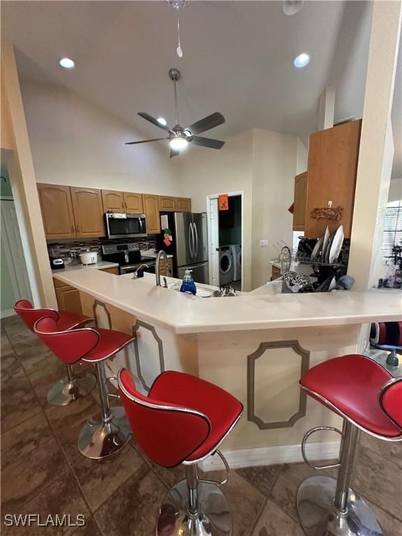 kitchen with high vaulted ceiling, a kitchen breakfast bar, kitchen peninsula, stainless steel appliances, and washer / clothes dryer