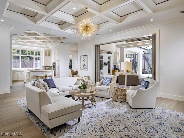 living room with ceiling fan with notable chandelier, light wood-type flooring, crown molding, and coffered ceiling