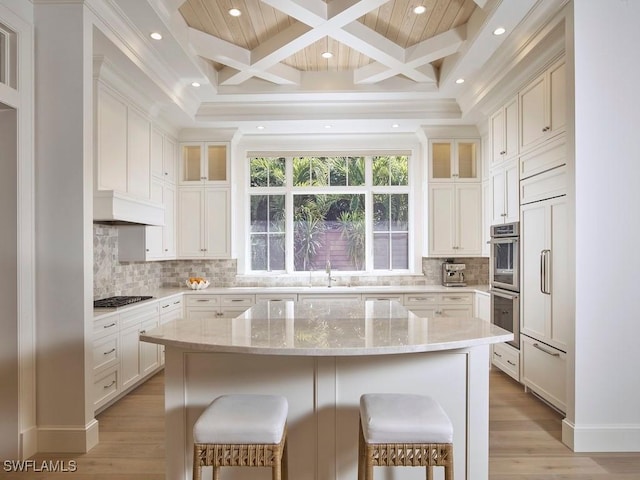 kitchen featuring light stone countertops, coffered ceiling, a kitchen island, beamed ceiling, and white cabinets