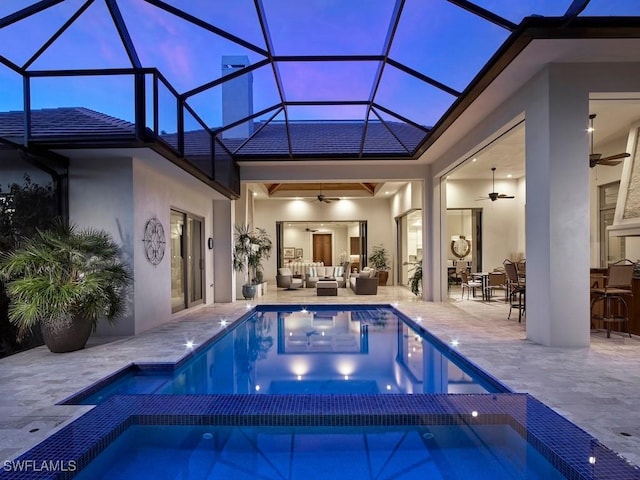 pool at dusk with ceiling fan, an outdoor living space, an in ground hot tub, and glass enclosure