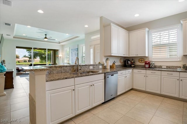 kitchen with a raised ceiling, white cabinetry, dishwasher, and dark stone counters