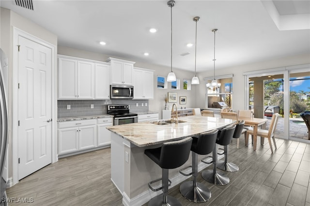 kitchen with light stone countertops, stainless steel appliances, sink, decorative light fixtures, and white cabinets