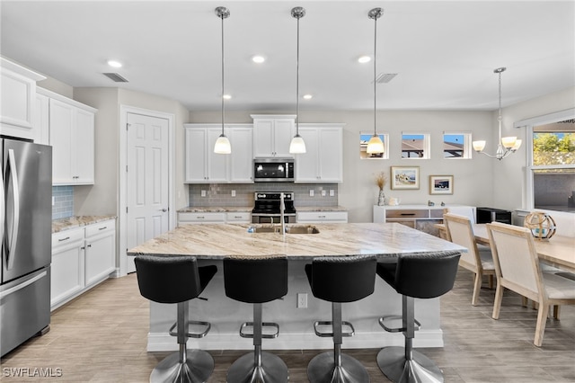 kitchen with a kitchen island with sink, hanging light fixtures, light stone countertops, appliances with stainless steel finishes, and white cabinetry