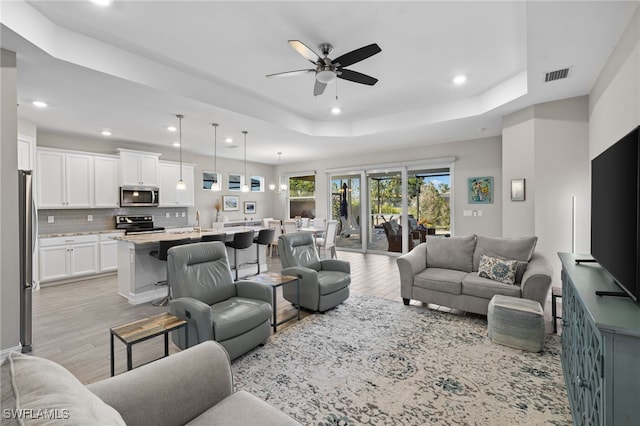 living room with a tray ceiling, ceiling fan, light hardwood / wood-style flooring, and sink