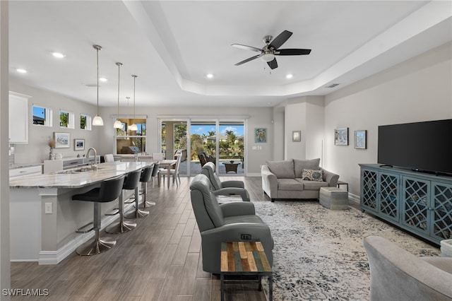 living room featuring a raised ceiling, ceiling fan, and sink