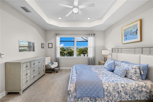 carpeted bedroom with a raised ceiling and ceiling fan