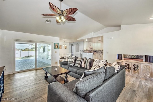 living room with ceiling fan, light hardwood / wood-style floors, and vaulted ceiling