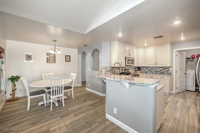 kitchen with light hardwood / wood-style floors, washer / dryer, kitchen peninsula, and stainless steel appliances