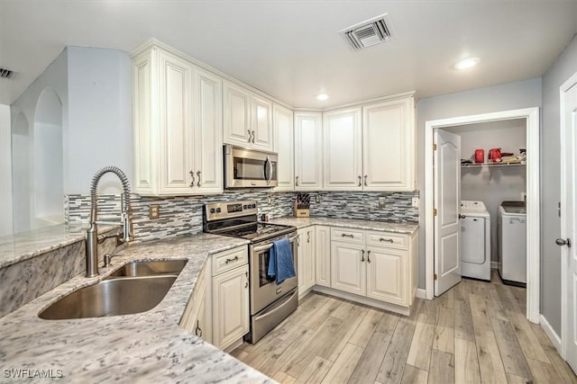 kitchen featuring sink, stainless steel appliances, separate washer and dryer, light stone counters, and light wood-type flooring