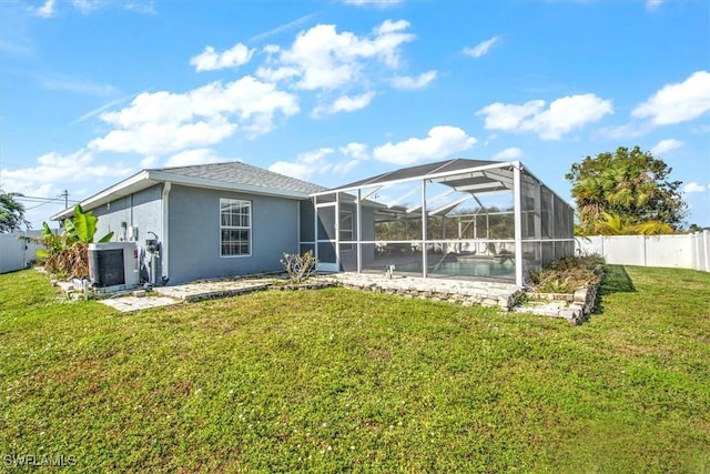 back of property with central AC unit, glass enclosure, and a yard