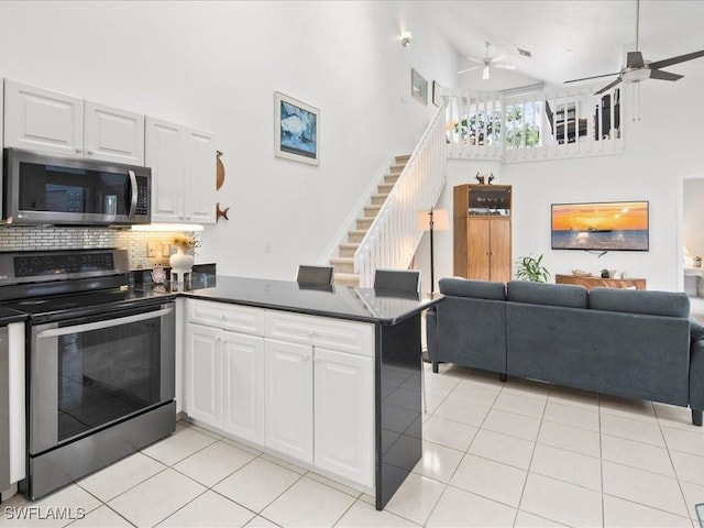 kitchen featuring kitchen peninsula, white cabinetry, a towering ceiling, and appliances with stainless steel finishes