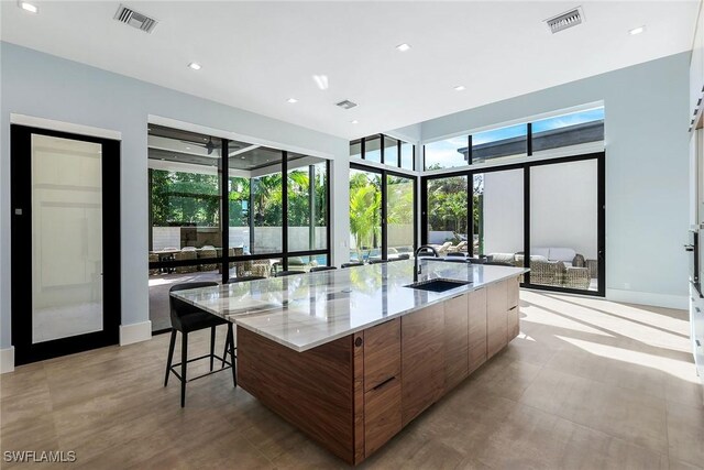 kitchen with a large island with sink, light stone countertops, sink, and a breakfast bar