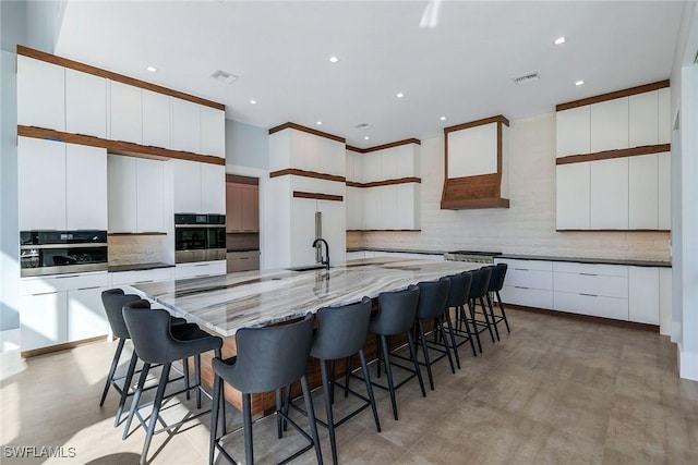 kitchen with a large island with sink, white cabinetry, oven, and a breakfast bar area