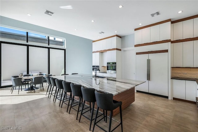 kitchen with light stone countertops, a large island, built in refrigerator, oven, and white cabinets