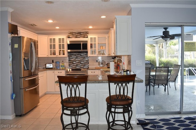 kitchen featuring ceiling fan, dark stone countertops, a breakfast bar area, white cabinets, and appliances with stainless steel finishes