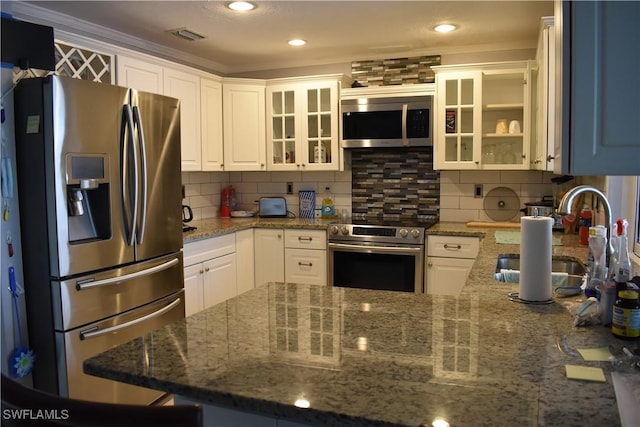 kitchen featuring ornamental molding, stainless steel appliances, sink, dark stone countertops, and white cabinetry