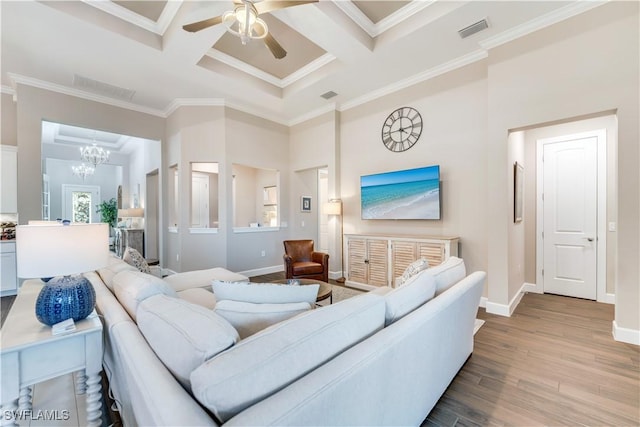 living room with ceiling fan with notable chandelier, light hardwood / wood-style floors, crown molding, and coffered ceiling