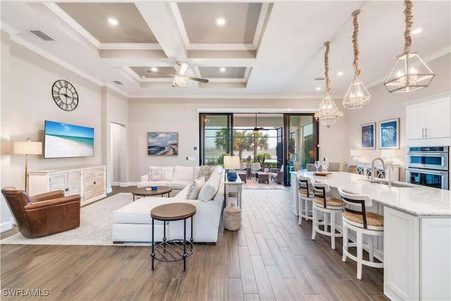 living room featuring sink, coffered ceiling, dark hardwood / wood-style flooring, ceiling fan with notable chandelier, and ornamental molding