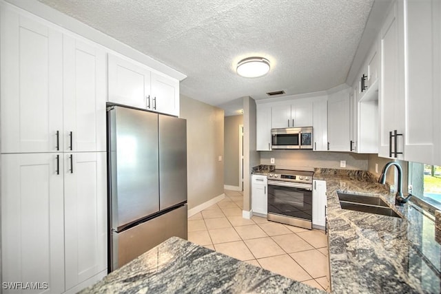 kitchen featuring dark stone counters, sink, a textured ceiling, appliances with stainless steel finishes, and white cabinetry