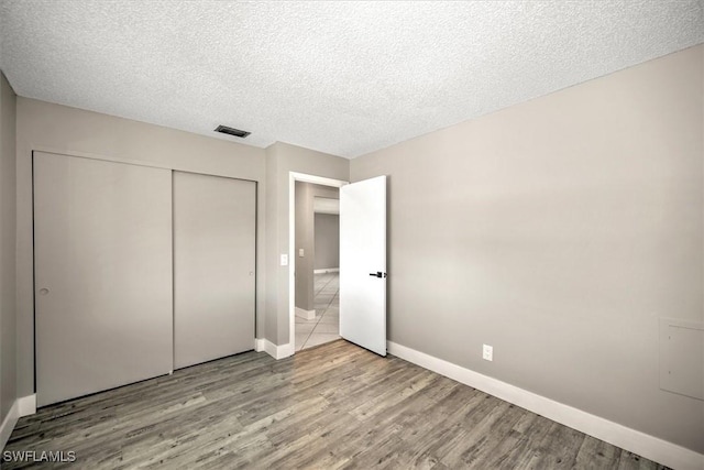 unfurnished bedroom with a textured ceiling, light hardwood / wood-style floors, and a closet