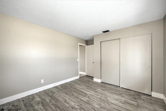 unfurnished bedroom with light wood-type flooring, a textured ceiling, and a closet