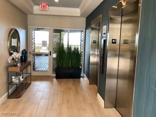 doorway to outside with elevator, a raised ceiling, and light hardwood / wood-style flooring