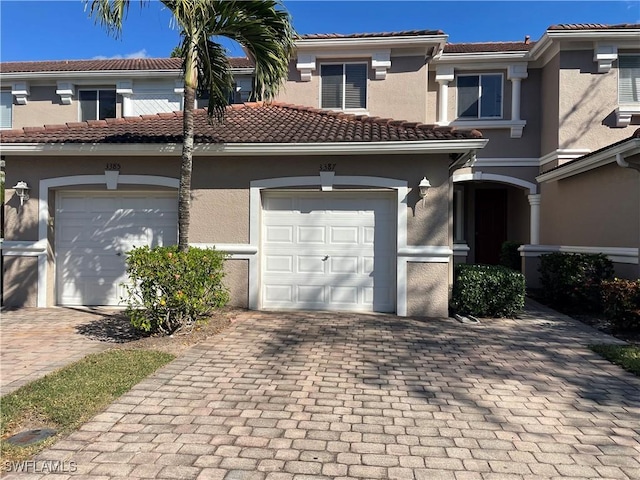 townhome / multi-family property with a tiled roof, decorative driveway, an attached garage, and stucco siding