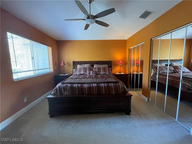 bedroom with ceiling fan, light carpet, and two closets