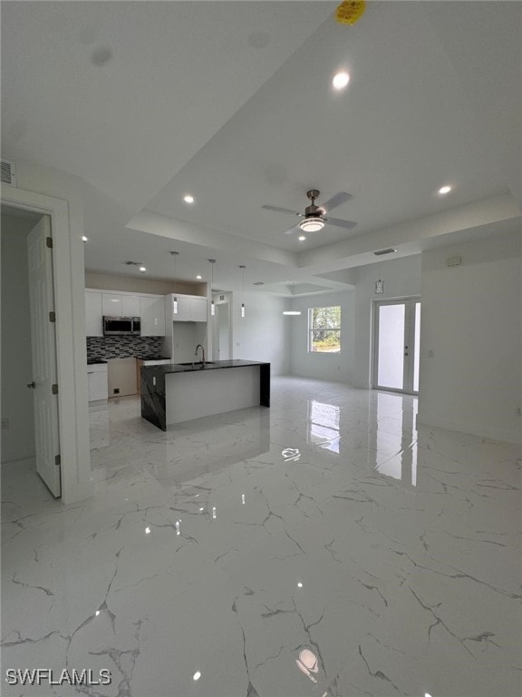 kitchen with decorative backsplash, a raised ceiling, sink, white cabinetry, and an island with sink