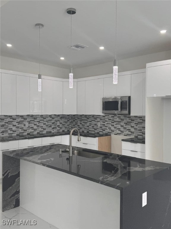 kitchen with pendant lighting, decorative backsplash, white cabinets, and dark stone countertops