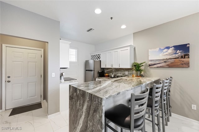 kitchen featuring a kitchen bar, stainless steel fridge, kitchen peninsula, tasteful backsplash, and white cabinets