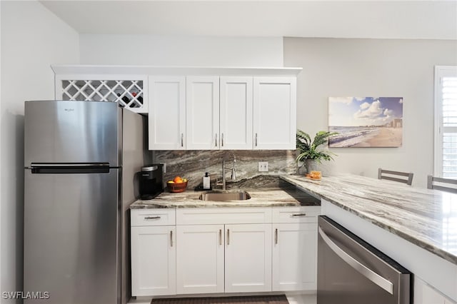 kitchen with light stone countertops, sink, white cabinets, and stainless steel appliances