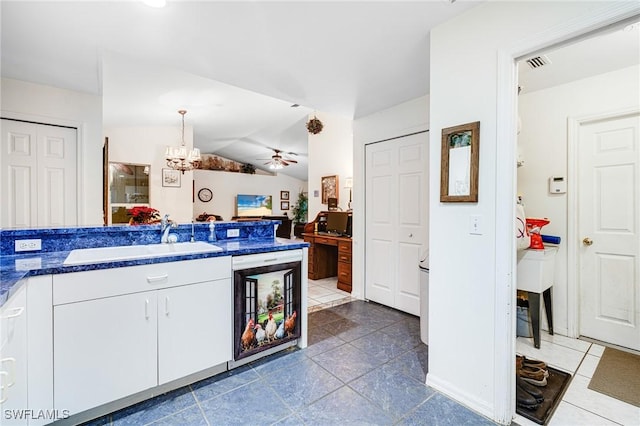 kitchen with white cabinetry, sink, pendant lighting, vaulted ceiling, and ceiling fan with notable chandelier