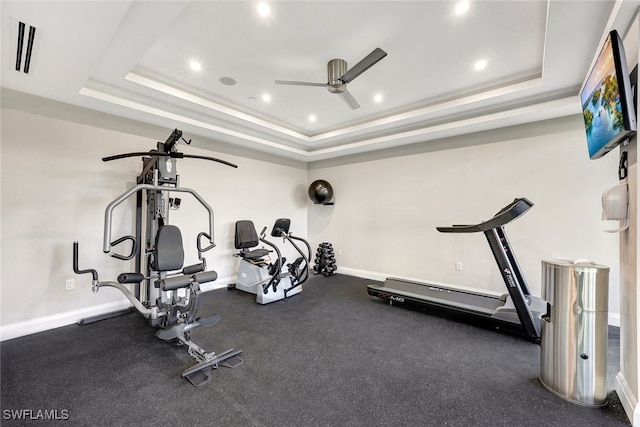 exercise room with ceiling fan and a tray ceiling