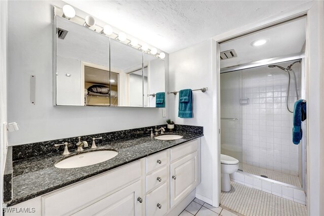 bathroom featuring vanity, a textured ceiling, tiled shower, tile patterned flooring, and toilet