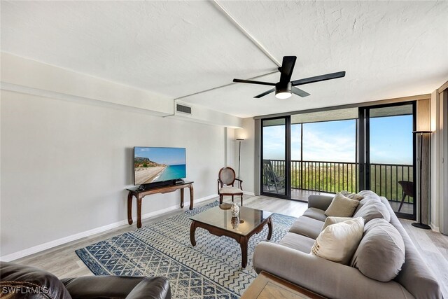 living room with ceiling fan, light hardwood / wood-style flooring, floor to ceiling windows, and a textured ceiling