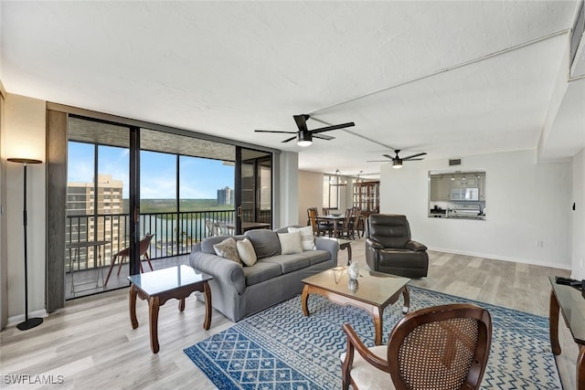 living room featuring ceiling fan, a wall of windows, and light hardwood / wood-style flooring