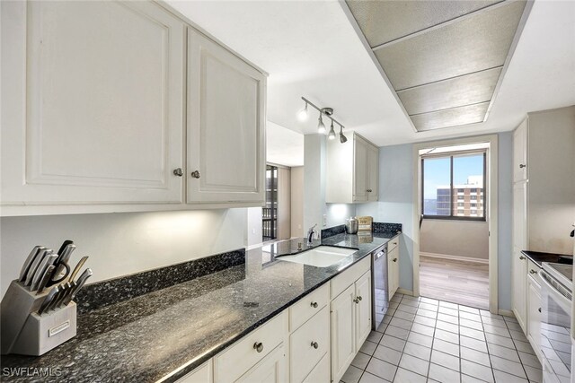 kitchen with dishwasher, sink, light tile patterned floors, dark stone countertops, and white cabinets