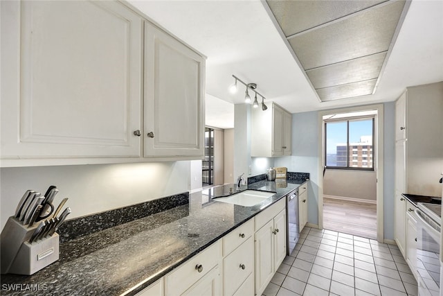 kitchen featuring light tile patterned flooring, sink, white cabinets, dark stone counters, and stainless steel dishwasher