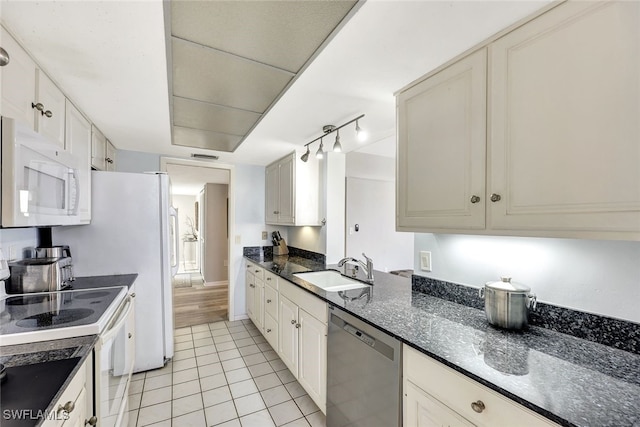 kitchen with light tile patterned flooring, sink, white cabinetry, dark stone countertops, and white appliances