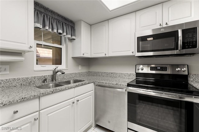 kitchen with appliances with stainless steel finishes, white cabinets, light stone counters, and sink