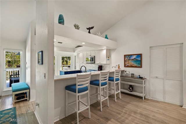 kitchen with a breakfast bar, tasteful backsplash, kitchen peninsula, light hardwood / wood-style floors, and white cabinets