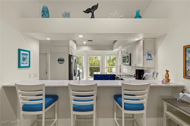 kitchen featuring a breakfast bar, stainless steel appliances, white cabinets, decorative backsplash, and kitchen peninsula