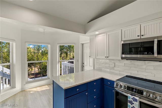 kitchen with blue cabinetry, lofted ceiling, white cabinetry, light stone counters, and appliances with stainless steel finishes