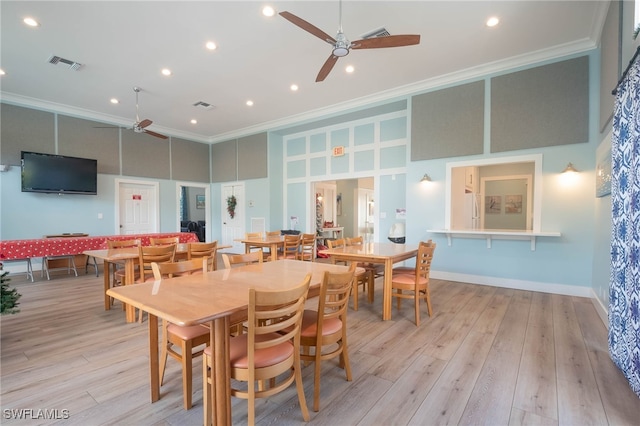 dining space with ceiling fan, light hardwood / wood-style floors, a high ceiling, and ornamental molding