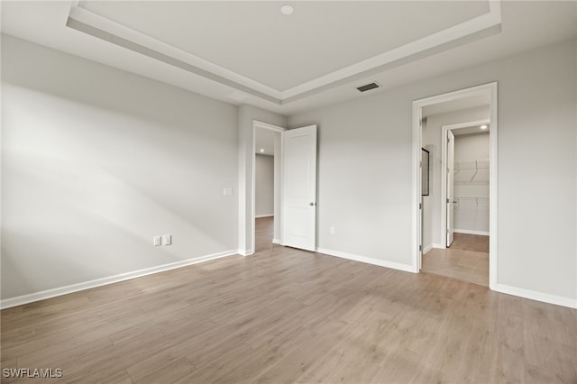 unfurnished bedroom featuring light hardwood / wood-style floors, a walk in closet, a closet, and a tray ceiling