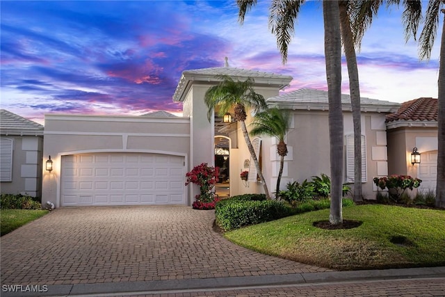 mediterranean / spanish home with stucco siding, decorative driveway, a yard, and an attached garage