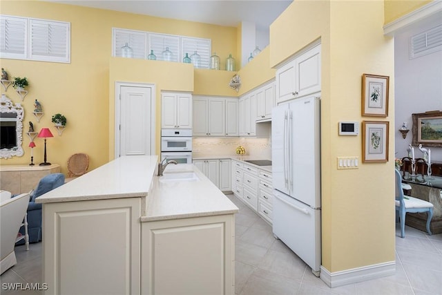 kitchen featuring white cabinetry, sink, an island with sink, white appliances, and decorative backsplash