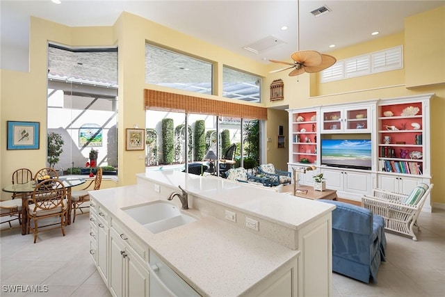 kitchen with light stone countertops, ceiling fan, sink, a center island with sink, and white cabinets