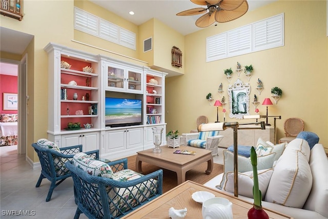 living area featuring baseboards, visible vents, a high ceiling, light tile patterned flooring, and ceiling fan